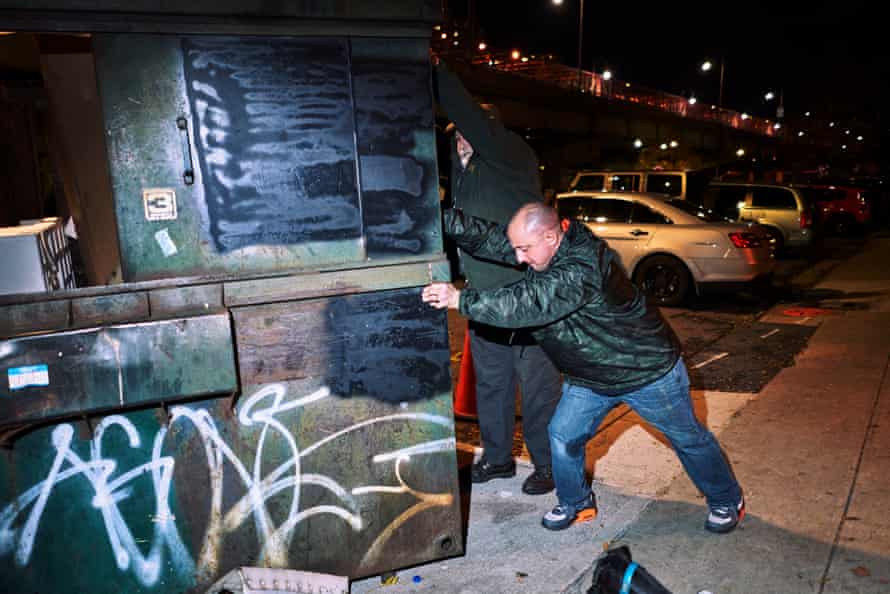 Jimmy Hoffman, front, and Richard Reynolds, back, shake a large garbage container to get the rats to come out in the Lower East Side.