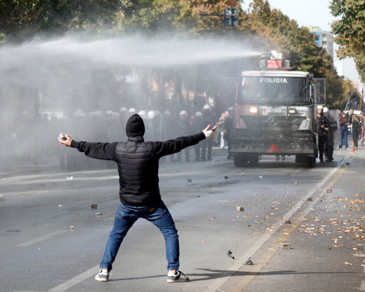A protesters stands in the street facing a water cannon