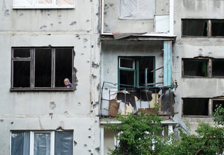 A woman stares out of her window of her flat in Sloviansk. A balcony is destroyed and the walls are covered in dents in the masonry.