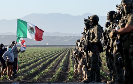 Federal agents with weapons block people protesting an Ice raid at a cannabis farm