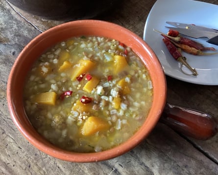Pumpkin, barley and lentil soup in a bowl, with chillies alongside.