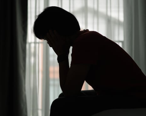 Silhouette of a person sitting with head in hand by window