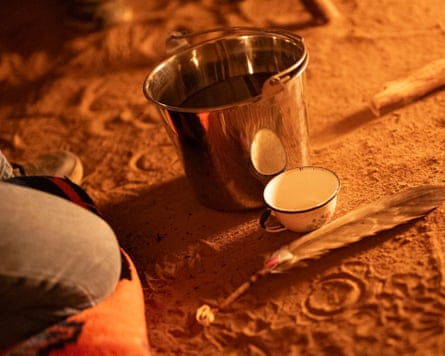 A bucket of peyote tea on the floor with a cup next to it