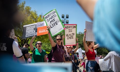 women at a protest with signs saying 'abortion saved my life' and 'abortion is health care'