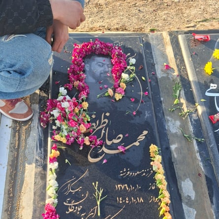 Grave of a man in Behesht-e Zahra cemetery in Tehran, with an image of the man engraved in the black stone, gold Persian lettering and flowers strewn around.