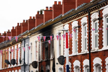 A burnt out house in a terrace of housing with union flag bunting hung across the street
