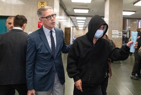a man in a suit guides a man in a hoodie and a face mask in a court building