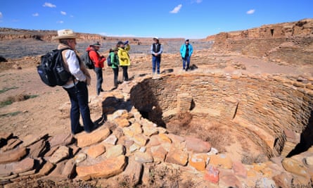 A guide talks to visitors beside an excavated kiva in the ruins of a massive stone complex (Pueblo Bonito) at Chaco Culture National Historical Park.