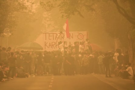 Protesters gather in thick haze with banners and the Indonesian flag over forest fires