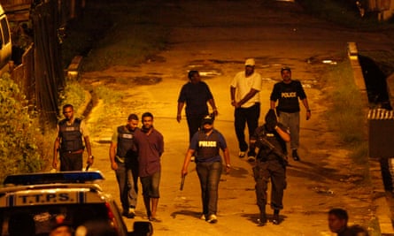 A team of police officers walk along a street as they return to their vehicles with a suspect in La Romaine, south Trinidad