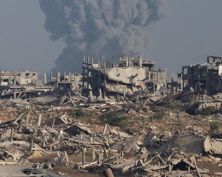 A huge plume of grey smoke rises behind a devastated landscape of destroyed buildings
