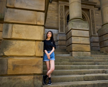 Chloe Cheung stands on stone steps, leaning against the stone wall of the town hall