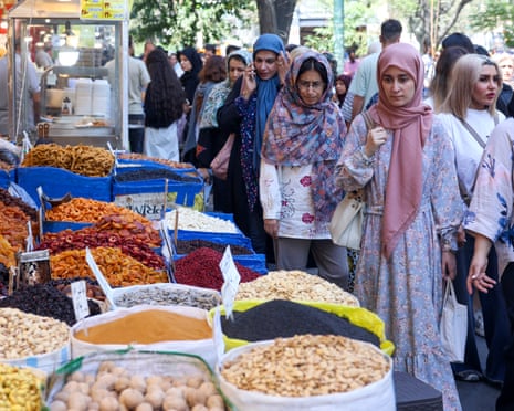 Women browse a Tehran market stall piled with dried fruits, nuts, and spices