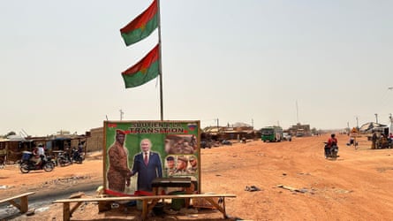 A advertising board with a poster of the presidents of Russia and Burkina Faso shaking hands on a dirt road