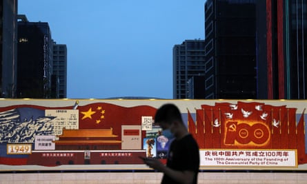A man walks past a decorated board with images of Tiananmen Gate and Chinese national flag, marking the 100th founding anniversary of the CCP in Beijing
