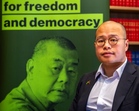 Sebastien Lai in front of a poster of Jimmy Lai with the words 'for freedom and democracy'