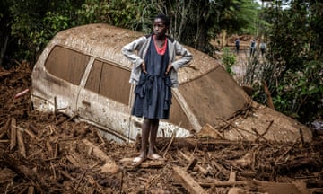A girl stands next to a damaged car buried in mud at an area heavily affected by torrential rains and flash floods in the village of Kamuchiri