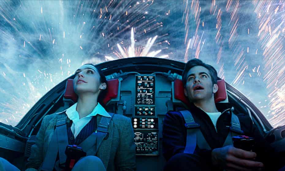 Gal Gadot and Chris Pine in  a futuristic vehicle, looking up through its canopy at fireworks exploding around them