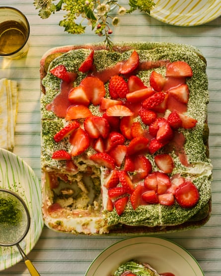 An oblong shaped pudding in a dish, covered in strawberries, with a slice taken out