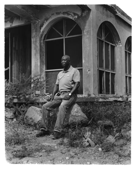 A man in a polo shirt and jeans sits on a rock outside a dilapidated with floor to ceiling arched windows