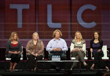 five people sit in a row onstage with the TLC logo behind them