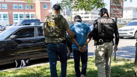 A handcuffed person, pinch backmost to nan camera, is walked towards a waiting car by 2 ICE agents astatine either side