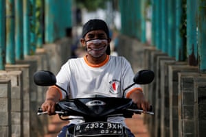 A man riding a motorbike in Jakarta, Indonesia, sports a smiley face mask