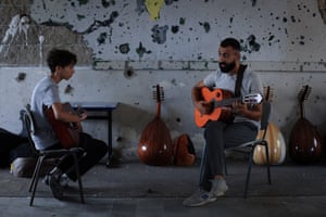 A man with a classical guitar teaches a teenager how to play