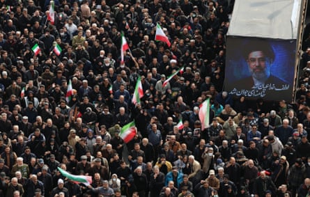 Aerial view of people standing around a poster of Mojtaba Khamenei, some holding Iranian flags