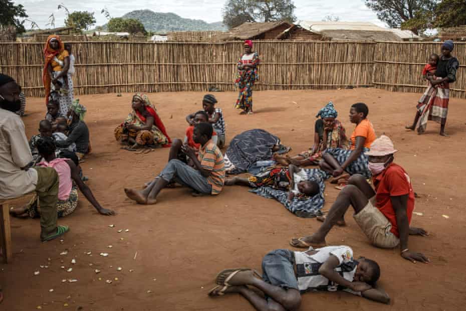 Displaced people sit and lie outside tents.