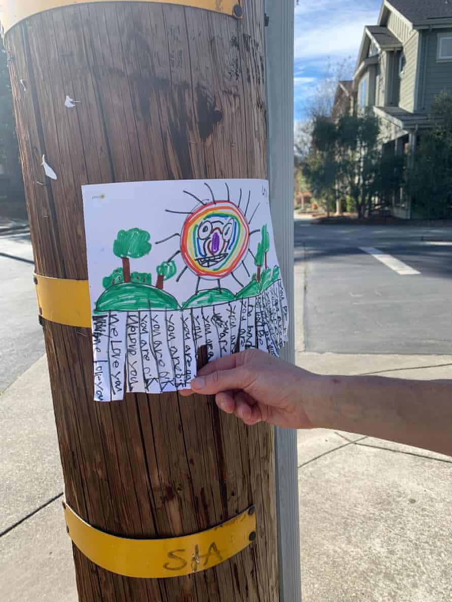 A poster on a telephone pole shows a drawing of a rainbow sun with positive messages that can be torn off.