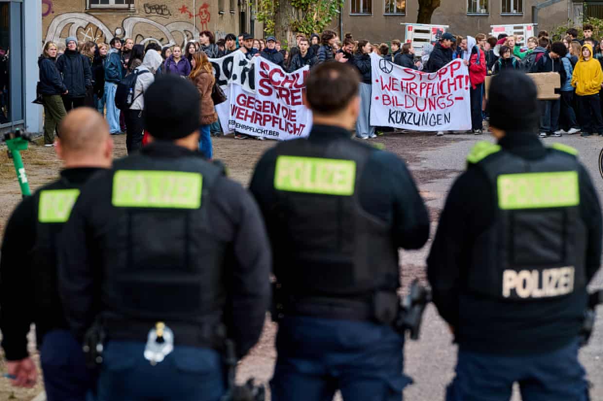 Police officers in riot gear face student protesters holding banners outside a school