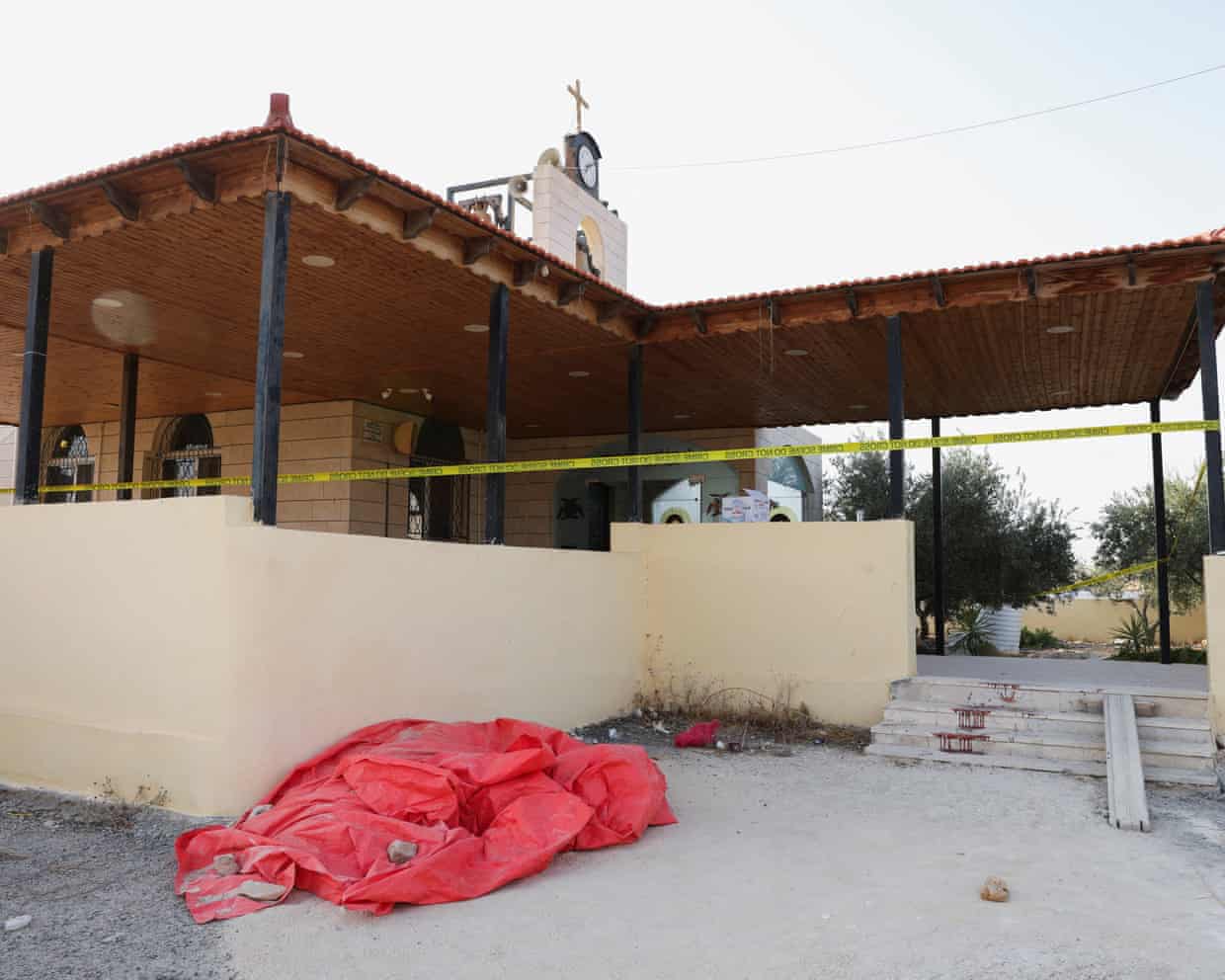A red tarp covers a shape outside Saint George’s church, cordoned with crime scene tape