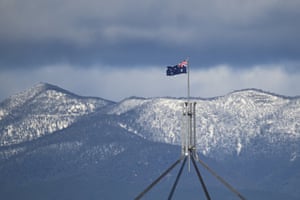The top of Parliament House is seen in front of snow-covered hills surrounding the Australian Capital Territory.