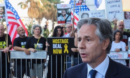 Blinken in foreground with people behind barrier with US flags and posters behind him