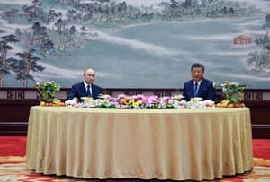The two leaders sitting at a large, formal round table covered in flowers and fruit with a beautiful painting behind them depicting a wintery nature scene