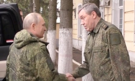 Vladimir Putin, wearing military camouflage, shakes hands with Valery Gerasimov