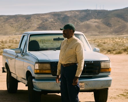 man in button down shirt and hat stands next to pickup truck outside