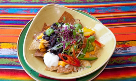 Nachos with lots of toppings on a pale yellow plate set on a colourful Mexican cloth