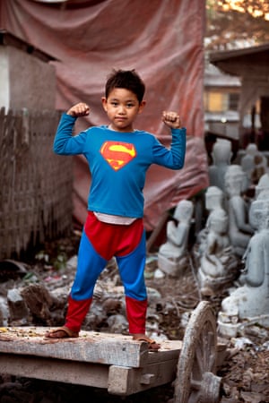 Boy flexiona seus músculos no distrito de escultura em mármore de Mandalay.