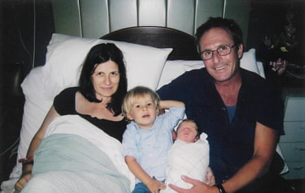 A mother and father with their toddler son, and their newborn daughter, sitting on a bed together.