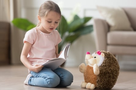 A girl reading a book to a toy hedgehog