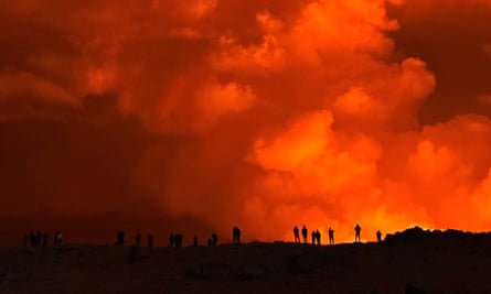 People silhouetted against the glow from a volcano as it erupts in Iceland, as seen from Keflavik.