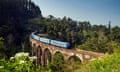 blue train on nine-arch bridge in lush countryside