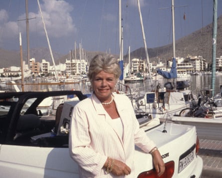 Chalmers in front of a white convertible car and yachts at a marina.