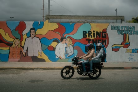 Two people on a moped ride past a brightly-coloured mural of Maduro and his wife bearing the words ‘bring them back’