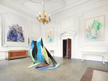 A grand, white-painted room with a chandelier, paintings on the wall and a metal sculpture in the middle of the floor