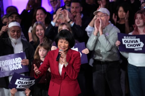 Olivia Chow in a red blazer speaks into a microphone before a cheering crowd holding campaign signs