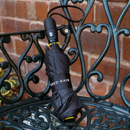 A folded black Shed Rain umbrella with yellow accents rests on an ornate metal railing