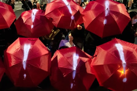 View from above of protesters holding open red umbrellas painted with white exclamation marks